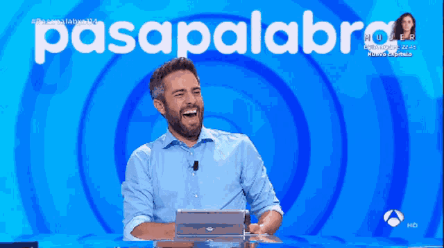a man laughs in front of a blue background that says pasapalabra