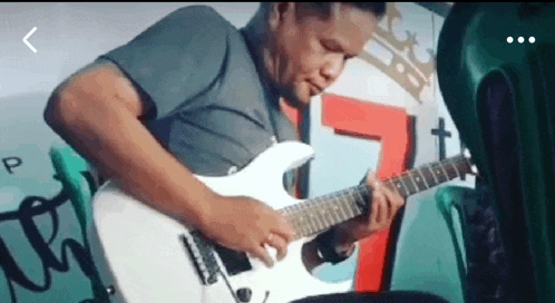 a man is playing a white electric guitar in front of a graffiti wall .