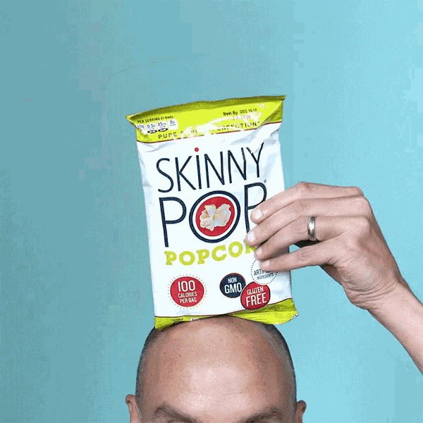 a bald man holds up a bag of skinny pop popcorn