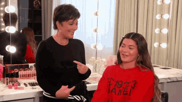 a woman is pointing at a girl wearing a red sweater that says 1973 chanel