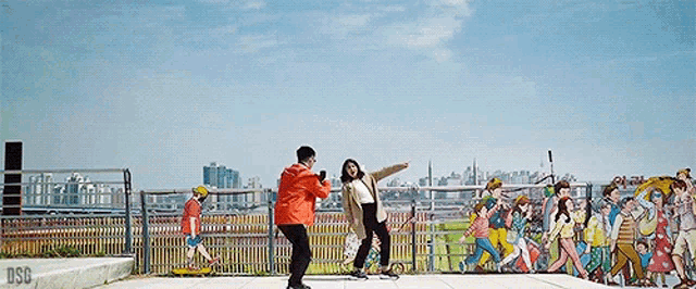 a man and a woman are posing for a picture in front of a fence with a city in the background .