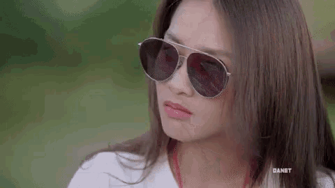 a woman wearing sunglasses and a white shirt is making a face .