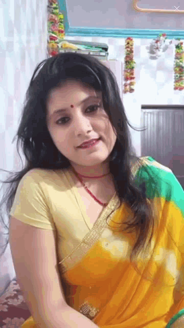 a woman in a yellow and green saree is sitting on a bed