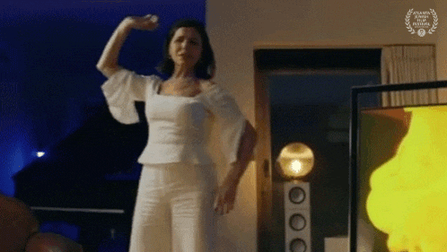 a woman in a white top and white pants is dancing in a living room