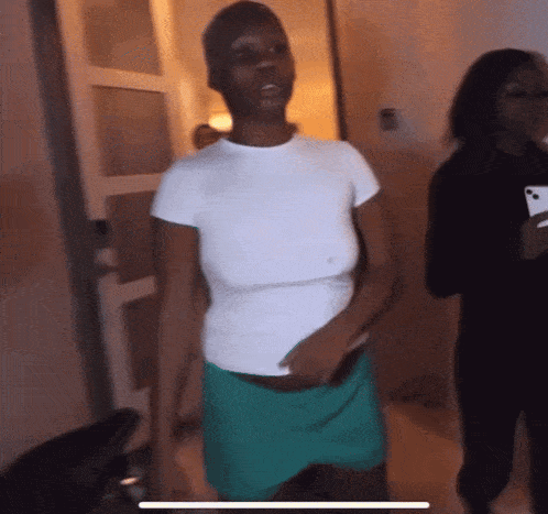 a woman in a white shirt and green shorts stands in a dark room