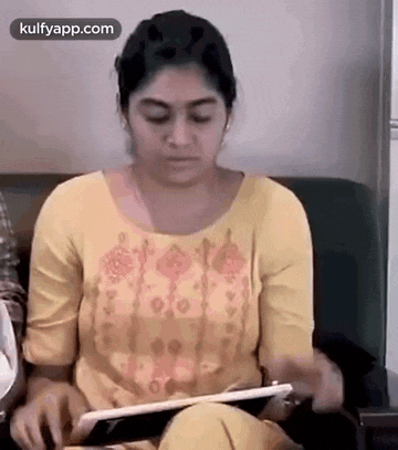 a woman in a yellow dress is sitting on a couch holding a tablet computer .