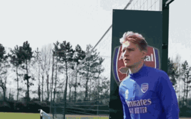 a soccer player wearing a blue emirates shirt stands in front of a sign .