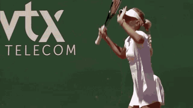 a woman is holding a tennis racquet in front of a vtx telecom sign
