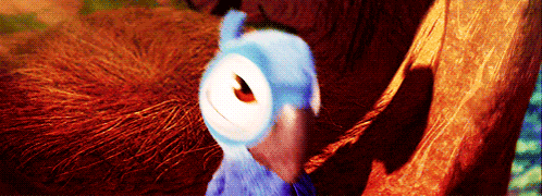a blue parrot is standing next to a tree branch and smiling