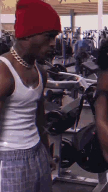 a man wearing a red hat and a white tank top is in a gym