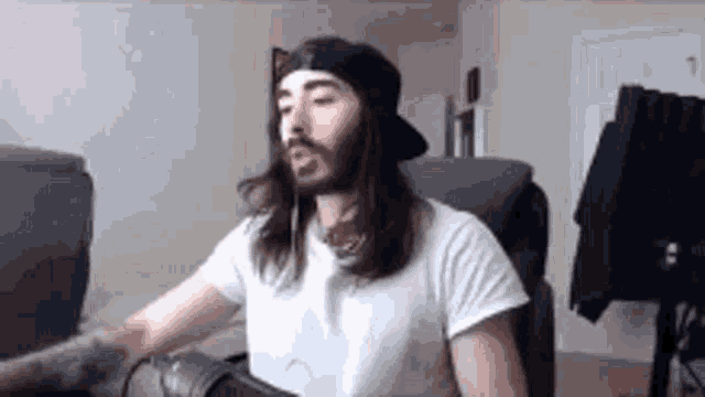 a man with long hair and a beard is sitting in front of a computer .