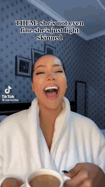 a woman in a white robe is holding a cup of coffee and laughing