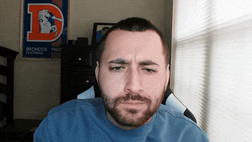 a man with a beard is sitting in front of a broncos football poster