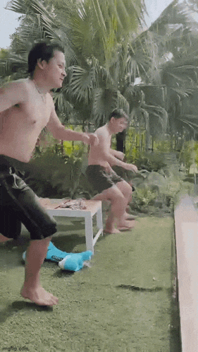 two men are jumping into a swimming pool while another man sits on a table .
