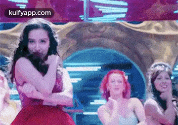 a woman in a red dress is dancing with a group of women in a room .