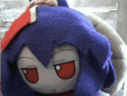 a stuffed animal with blue hair and red eyes is looking at the camera .