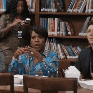 a woman in a blue shirt is sitting at a table in front of a bookshelf in a library .