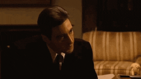 a man in a suit and tie is sitting on a couch and saying but your enemies closer .