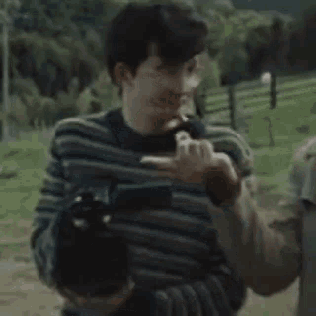 a man in a striped sweater is standing in a field holding a cigarette in his mouth .