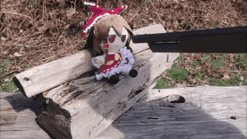 a stuffed doll is sitting on a piece of wood with a gun pointing at it