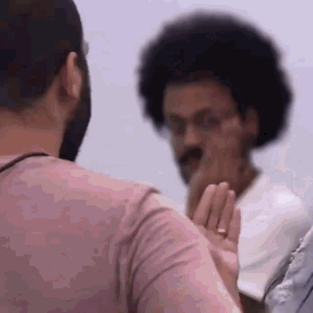 a man in a pink shirt is talking to another man in a white shirt with glasses .
