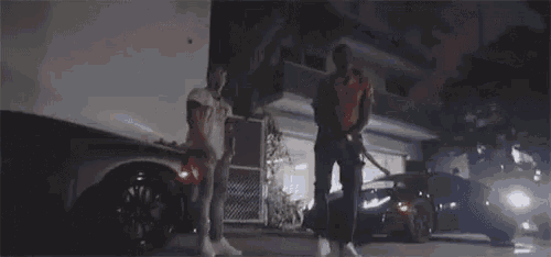 two men are standing next to each other in front of a building and a car .