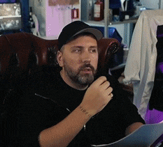 a man with a beard is sitting in a chair talking into a microphone while holding a piece of paper .