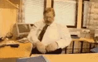 a man in a white shirt and tie is sitting at a desk with his legs crossed