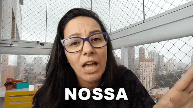 a woman wearing glasses says nossa in front of a balcony