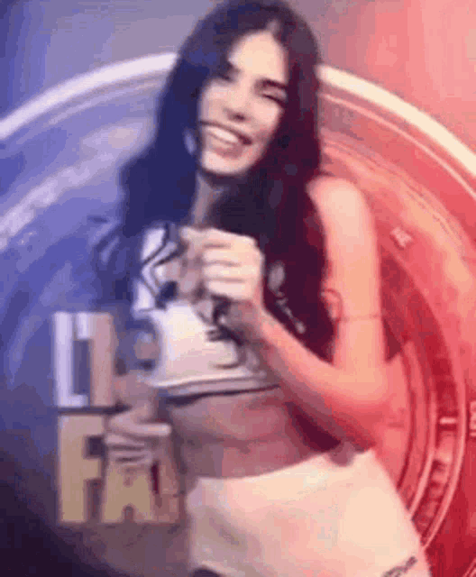 a woman in a crop top and shorts is smiling and holding a microphone in front of a circle .