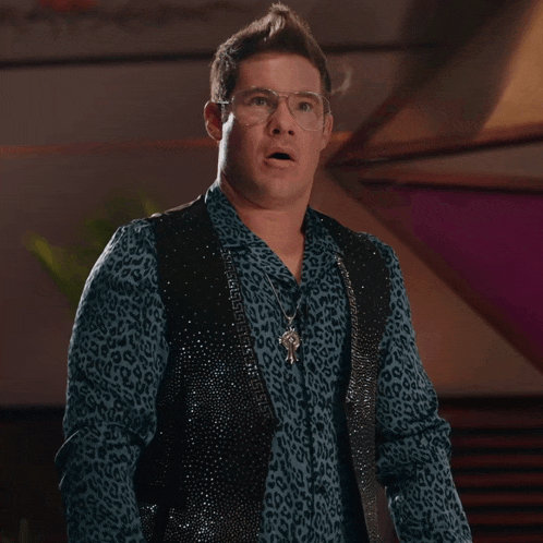 a man in a blue shirt and black vest is making a face .