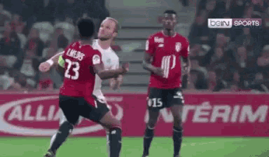a soccer player wearing a red jersey with the number 23 on it is fighting another player on the field .