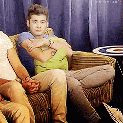 a man is sitting on a couch with his arms crossed and the hashtag fuckyeah1d is visible