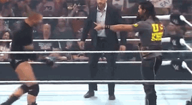 a man in a suit is standing in a wrestling ring talking to a wrestler .