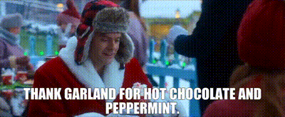 a man dressed as santa claus is sitting at a table with a cup of hot chocolate .