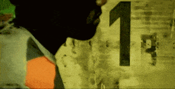a person in a mask stands in front of a wall with the number 1 on it