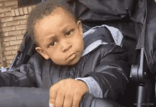 a young boy is sitting in a stroller and making a face .