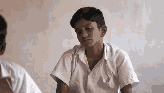 a boy in a white shirt sits in a dark room