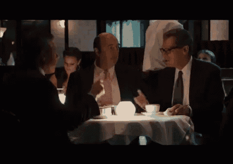 a man in a suit and tie sits at a table in a dark room