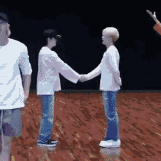 two men are shaking hands on a wooden floor while standing next to each other .