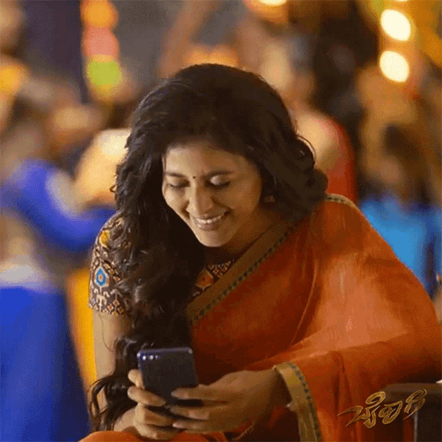 a woman in an orange saree is looking at her phone and smiling