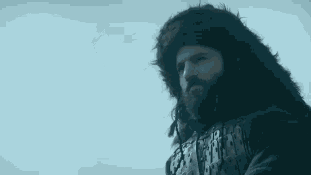 a man with a beard is wearing a fur hat and looking at the camera .