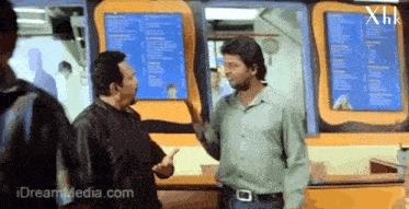 two men are talking in front of a menu that says ' xhk ' on it