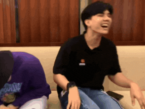 a man is sitting on a couch laughing while another man sits behind him .