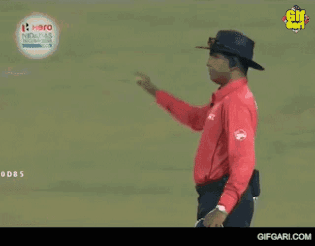 a man in a red shirt and black hat is pointing at a ball .