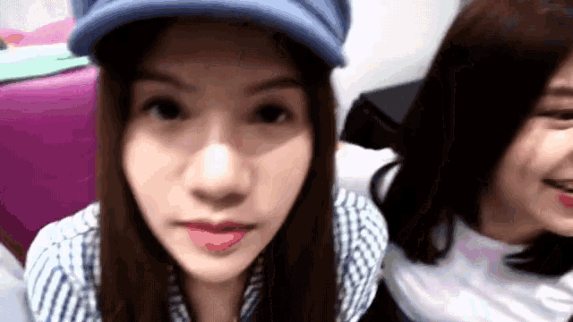 a woman wearing a blue hat looks at the camera while another woman looks on