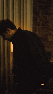 a man in a black jacket and glasses is standing in a dark room