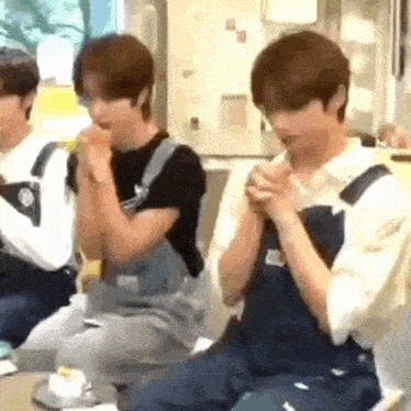 a group of young men wearing overalls are sitting at a table eating food .