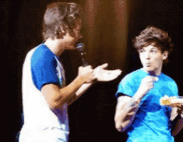 a man in a blue shirt is talking into a microphone while another man looks on