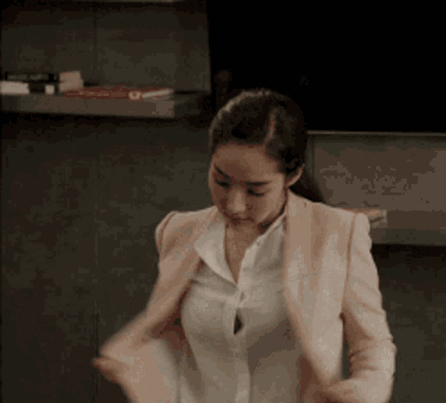 a woman wearing a white shirt and a pink jacket is taking off her jacket